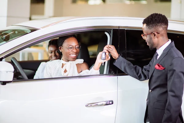 Situação de vendas na concessionária de automóveis, jovem casal africano recebe a chave para o carro novo — Fotografia de Stock