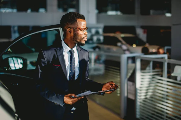 Handsome african car salesman standing at the dealership holding a tablet