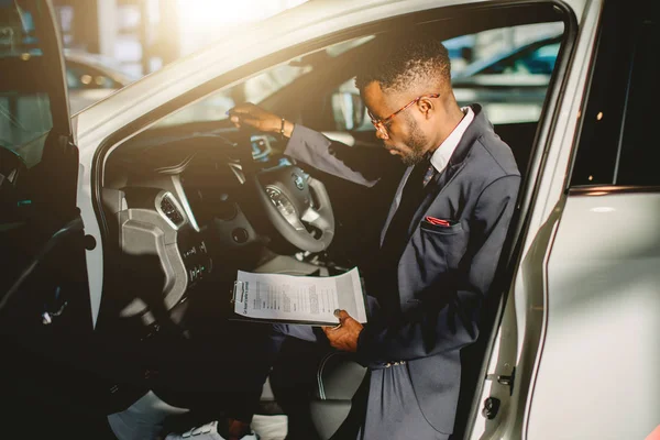 Schöner afrikanischer Autoverkäufer steht im Autohaus und hält ein Tablet in der Hand — Stockfoto