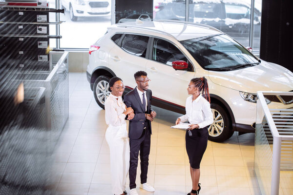 Продавец автомобилей, стоящий в салоне, рассказывает клиентам об особенностях автомобиля
