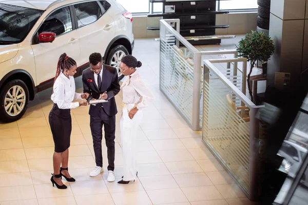 汽车推销员站立在经销商告诉关于汽车的特征对顾客 — 图库照片