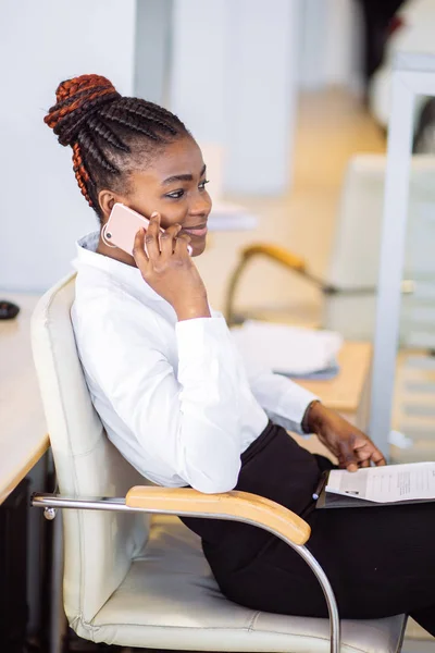 Africano mulher de negócios em vestido sentado à mesa e falando ao telefone no escritório — Fotografia de Stock