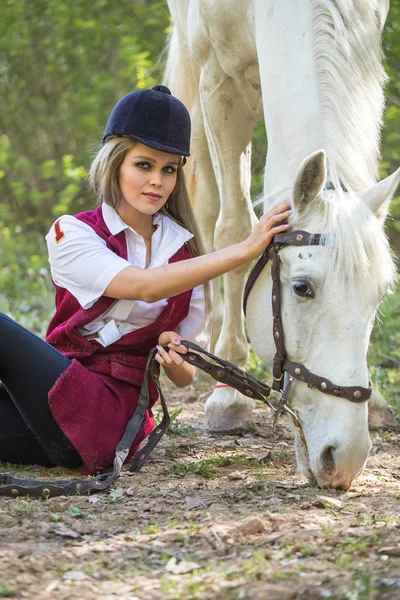 Mulher bonita sentada no chão com cavalo marrom perto dela . — Fotografia de Stock