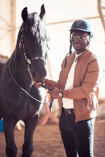 African Man wearing sunglasses near black horse in hangar — Stock Photo, Image