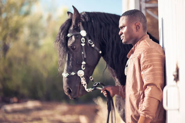 African Man wearing sunglasses near black horse in hangar — Stock Photo, Image