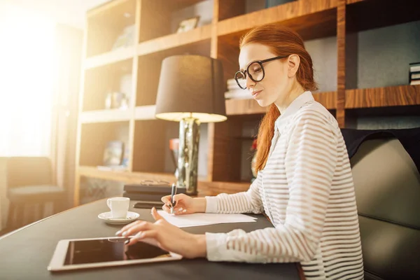 Frau schreibt mit digitalem Tablet-Computer im Büro auf Papier — Stockfoto