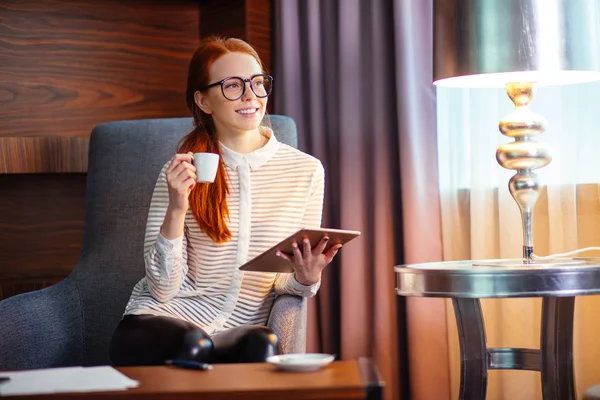 Woman drinking coffee and reading her tablet while standing in office — Stock Photo, Image