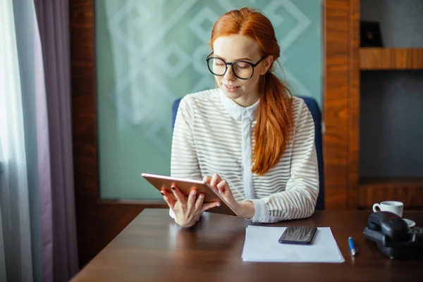 Roodharige lachende jonge vrouwelijke manager met behulp van moderne digitale tablet op kantoor — Stockfoto