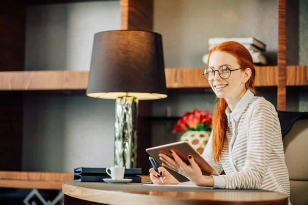 Рыжая улыбающаяся молодая женщина-менеджер, использующая современные цифровые планшеты в офисе — стоковое фото