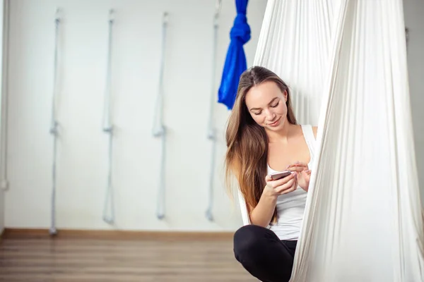 Женщина позирует в гамаке антигравитационной воздушной йоги. расслабиться с телефоном — стоковое фото