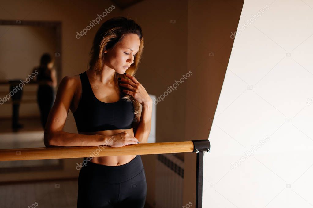 woman dancer posing near barre in ballet studio