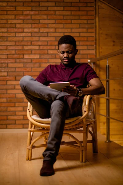 Homem africano usando tablet para conversa em vídeo enquanto relaxa na poltrona — Fotografia de Stock