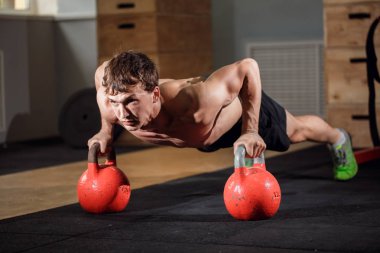 Young strong man doing push-ups on kettlebells clipart