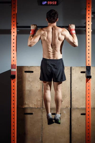 Atraente jovens adultos do sexo masculino fazendo pull ups no bar em cross fit ginásio de treinamento — Fotografia de Stock