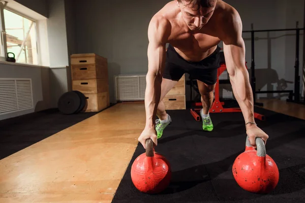 Jovem homem forte fazendo flexões em kettlebells — Fotografia de Stock