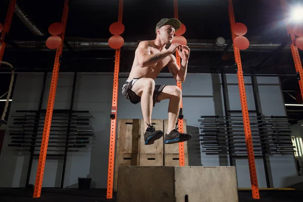 Чоловічий спортсмен коробка стрибає в поперечному положенні спортзалу. Підходить людина виконує стрибки коробки — стокове фото