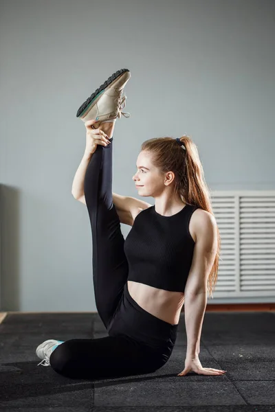 Hermosa morena delgada haciendo algunos ejercicios de estiramiento en un gimnasio — Foto de Stock