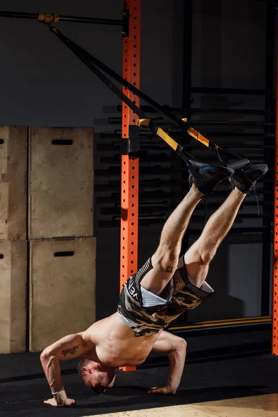 Mannelijke en atletische man doen trx oefeningen in een sportschool club bandjes. — Stockfoto