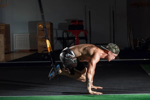 Usando bandas TRX, haciendo flexiones y rotaciones del torso con las piernas suspendidas . — Foto de Stock