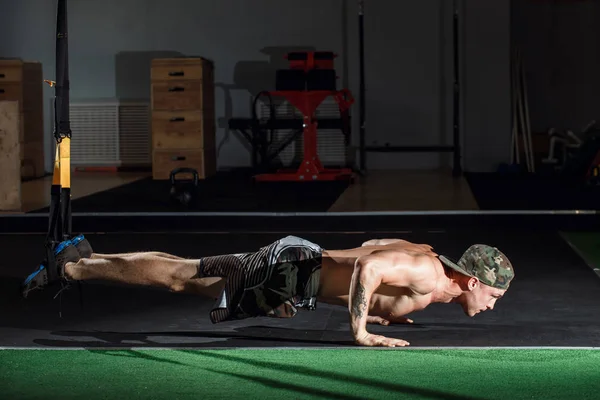 Mannelijke en atletische man doen trx oefeningen in een sportschool club bandjes. — Stockfoto