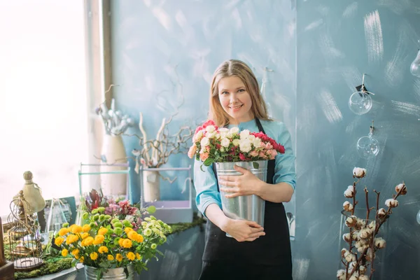 Glada blond florist står nära fönstret med blommor — Stockfoto