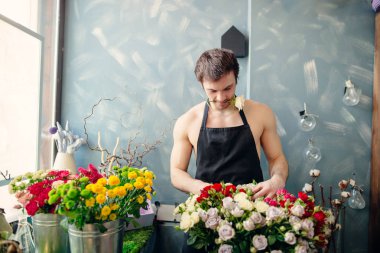 beyaz gül ağzına tutarak çiçek dükkanında çalışan adam