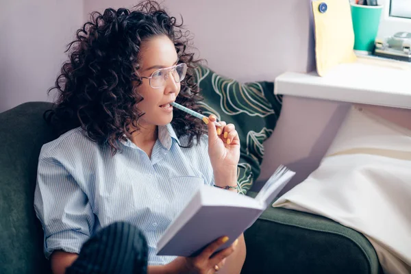 stock image side view shot of woman having pencil on mouth and holding book indoors