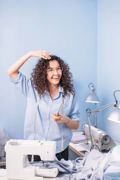 Schattig naaister tiding haar haar voor de tabel met kleermakers tools — Stockfoto
