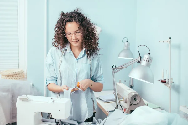 Bonita costurera con gafas de corte de tela para el vestido en el estudio de diseño —  Fotos de Stock