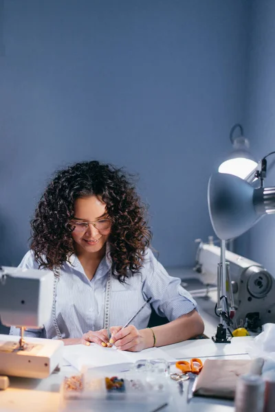 Naaister schrijven prijzen van clothers aan tafel in de donkere kamer verlicht met lamp — Stockfoto