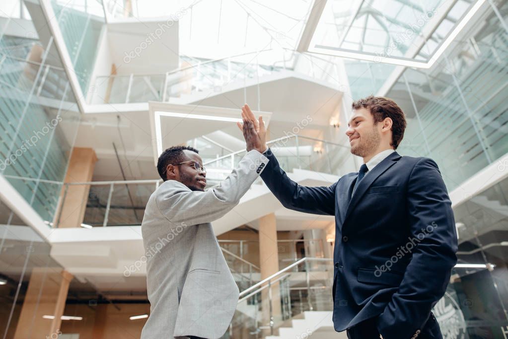 young colleagues giving each other high five while standing in an office