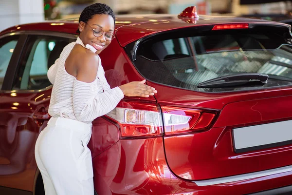 Sorrindo mulher africana abraçando carro vermelho no novo showroom carro — Fotografia de Stock