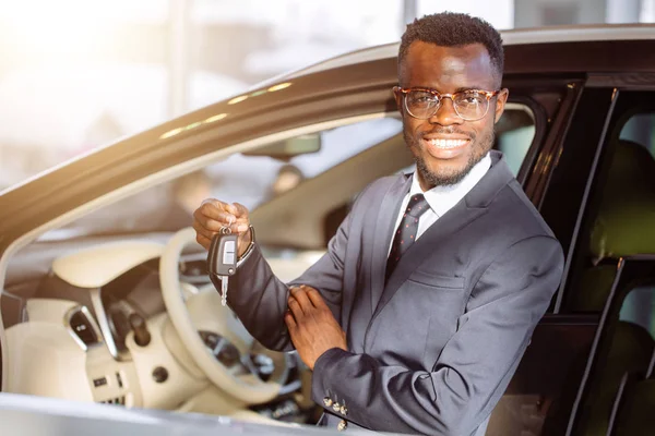 Jovem empresário africano sentado em um carro mostrando chave do carro — Fotografia de Stock