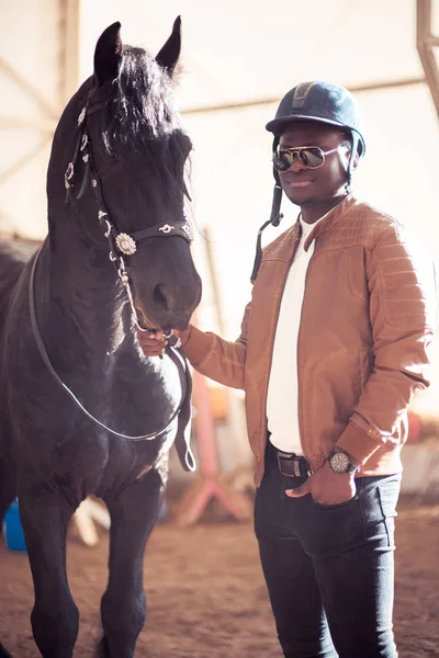 African Man wearing sunglasses near black horse in hangar — Stock Photo, Image