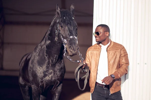 Afrikaner mit Sonnenbrille in der Nähe eines schwarzen Pferdes im Hangar — Stockfoto