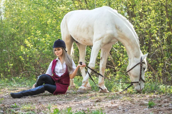 Schöne Frau auf dem Boden sitzend mit braunem Pferd in ihrer Nähe. — Stockfoto