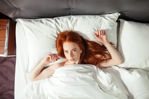 赤毛の女性は、ベッドと探してカメラであります。トップ ビュー — ストック写真