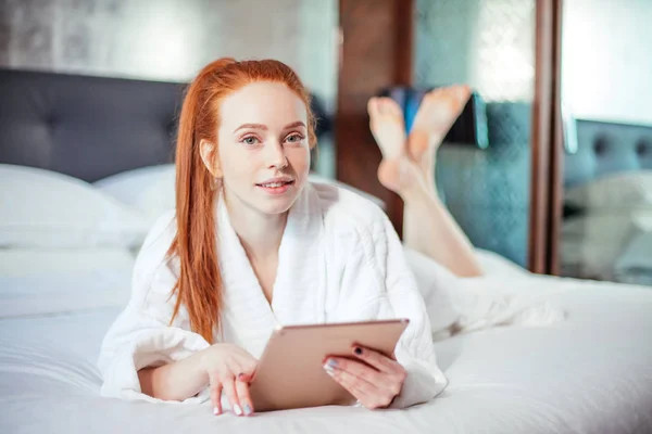 Schöne Frau im Bademantel und mit digitalem Tablet beim Entspannen auf dem Bett — Stockfoto