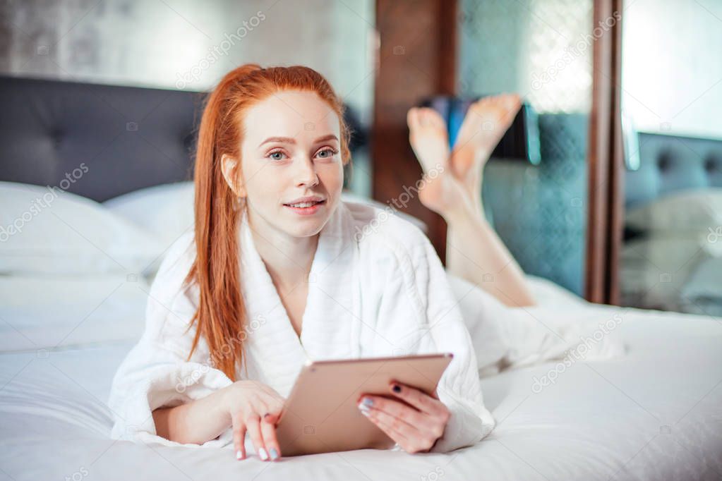 beautiful woman wearing bathrobe and using digital tablet while relaxing on bed