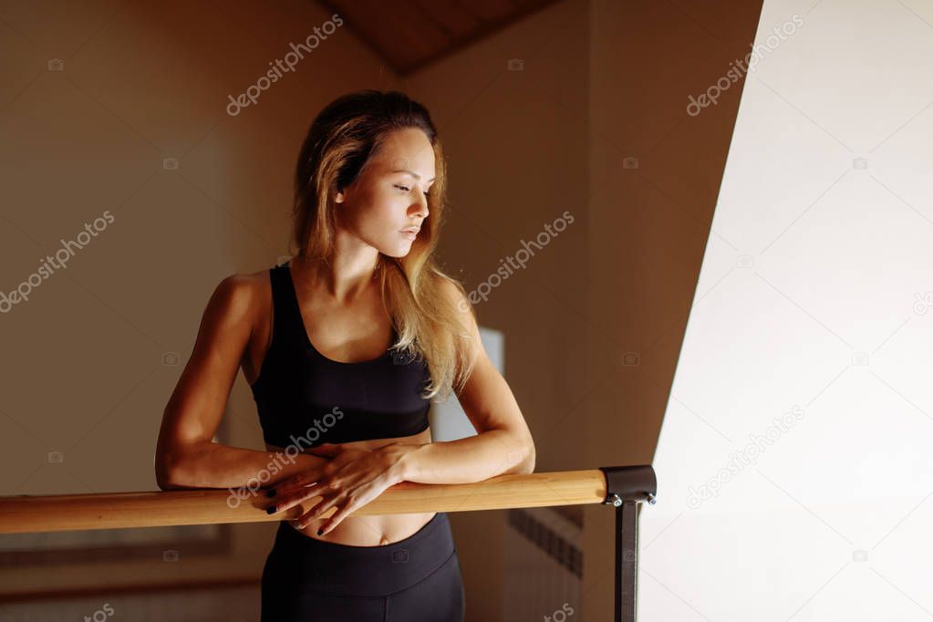 woman dancer posing near barre in ballet studio.