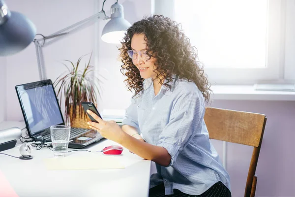 Chica atractiva charlando por teléfono delante de la computadora portátil en el trabajo — Foto de Stock