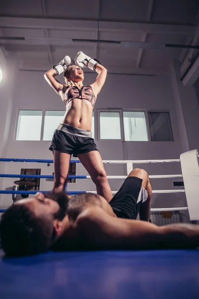 Baixo ângulo vista de mulher boxeador celebrando vitória, enquanto o homem deitado no chão anel — Fotografia de Stock