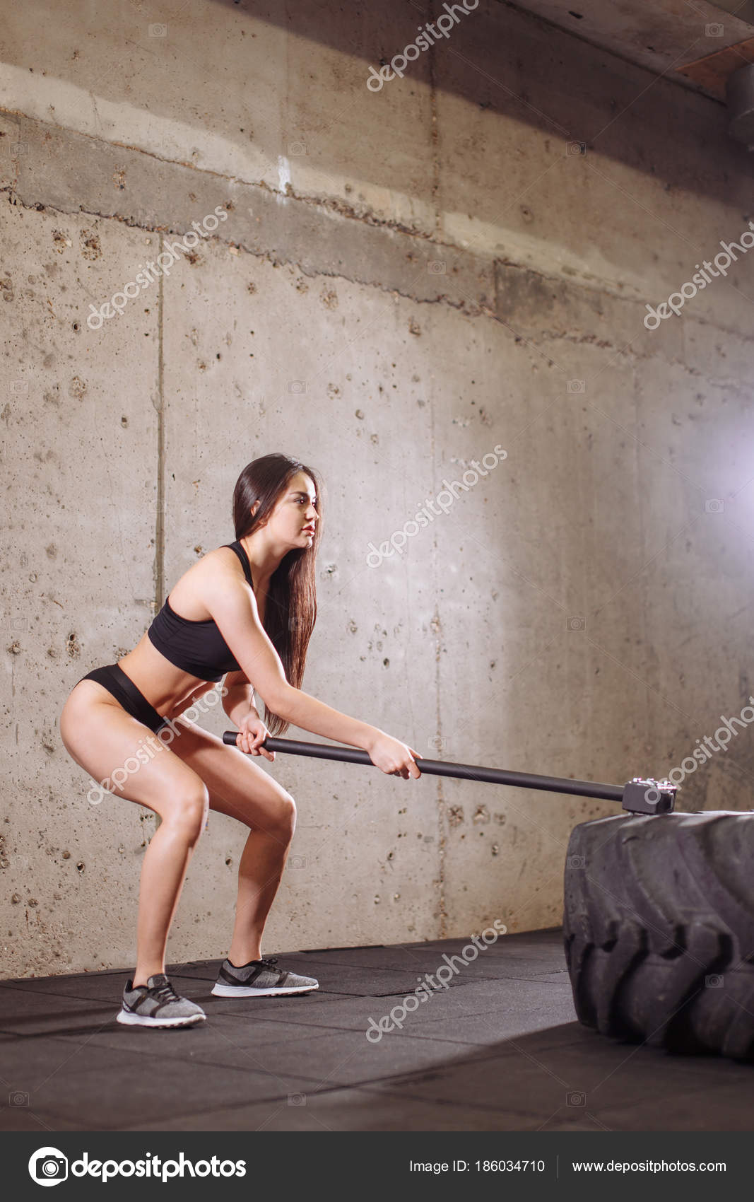 Woman smashing large tire with sledgehammer during intense workout in