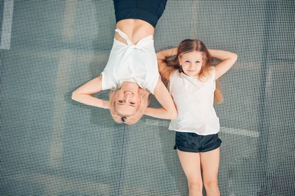 Moeder en dochtertje spelen in speeltuin en liggend op de trampoline — Stockfoto