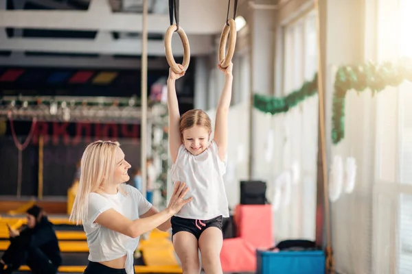 Matka dcera pomáhá sportovat na gymnastické kruhy — Stock fotografie