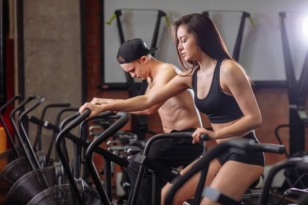 Femme et homme faisant du vélo dans la salle de gym, des jambes faisant de l'exercice cardio vélo d'entraînement — Photo