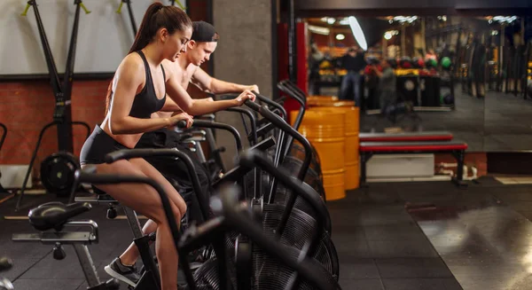 Mulher e homem de bicicleta no ginásio, exercitando as pernas fazendo bicicletas de ciclismo de treino cardio — Fotografia de Stock