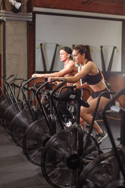 Γυναίκα και άνδρας ποδηλασία στο γυμναστήριο, άσκηση πόδια κάνουμε cardio προπόνηση ποδηλασίας ποδήλατα — Φωτογραφία Αρχείου