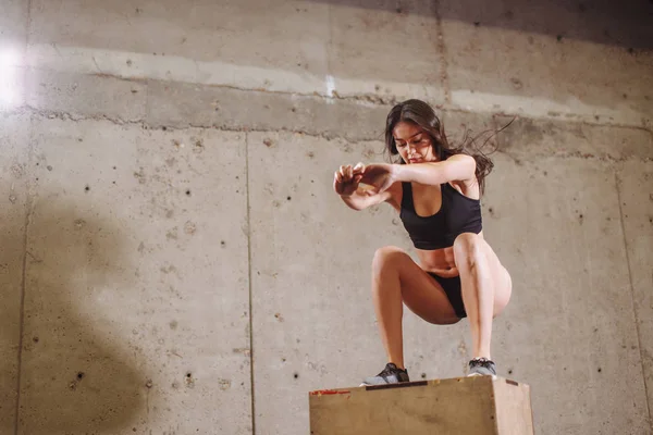 Mulher em forma fazendo um exercício de salto caixa. Mulher muscular fazendo um agachamento de caixa no ginásio — Fotografia de Stock