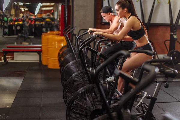 Vrouw en man fietsen in sportschool, uitoefening van benen doen cardio training fietsen Fietsen — Stockfoto